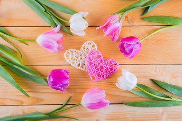 Bouquet of tender pink tulips with wicker hearts on light wooden background