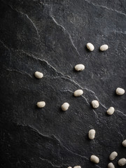 White beans are scattered randomly on a black stone table from slate.