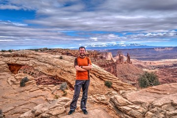 Bearded hipster man smiling on cliff with canyon views. Mesa Arch in Canyonlands National Park. Moab. Cedar City. La Sal Mountains.  Utah. United States.
