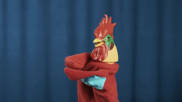 Comical red rooster hand puppet toy appear on scene making money bills or cards tossing gesture with blue crease curtains background