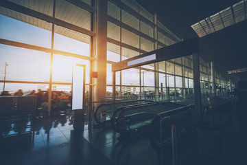 Moving staircase in hall of modern airport terminal with multiple passengers and taxis on street, interior of airport with escalator going down, huge window with cabstand, people and bus stop outside