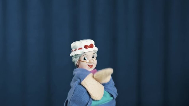 Old woman hand puppet appears on scene make tossing movements on blue crease curtains background on scene