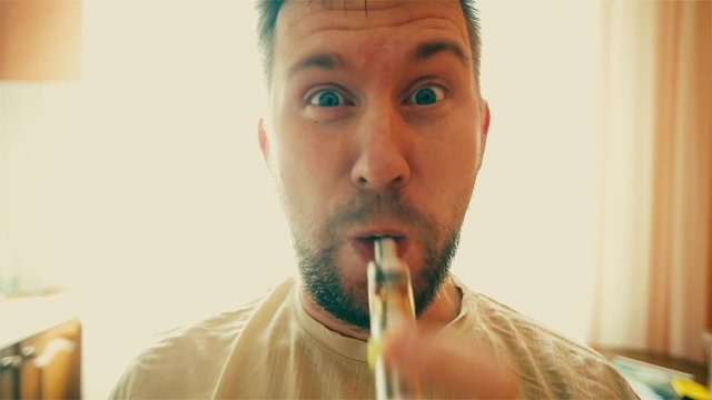 Young funny white man with beard and mustache admits puffs of steam from the electronic cigarette in the kitchen. Close up.