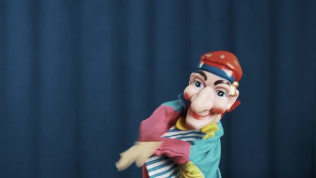 Petrushka hand puppet toy making money bills or cards tossing gesture on scene with blue crease curtains background