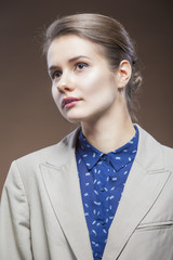 Natural Beauty portrait of Young Caucasian Girl in Pale Jacket and Blue Shirt Looking Forward.Against Brown Background
