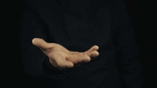 Caucasian male hand in long sleeve jacket making cash sign gesture rubbing fingers together on black background, close up isolated