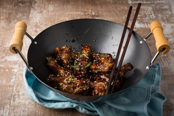 Chicken wings in a Chinese wok. Rustic wooden background 