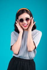 Full body of smiling asian woman dressed in pin-up style dress wearing eyeglasses over blue.