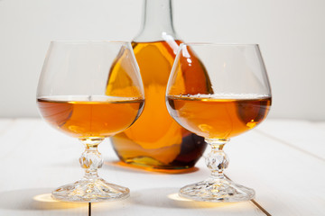 Glasses with cognac and a bottle on  white wooden background