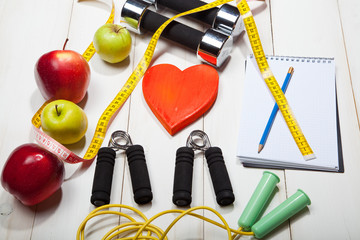 Heart, dumbbells and fruits, apples, oranges on a white wooden background