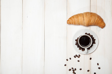Cup of coffee and a croissant on a white wooden table