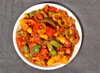 Indian style tricolour shimla mirch ki Sabzi (spicy capsicum vegetable) in white plate on black background.