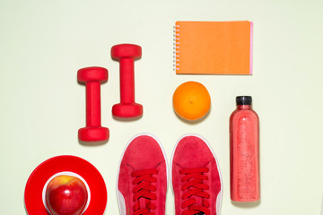 Fitness concept. Sneakers, apple, dumbbell and fruit juice bottle on pastel color background.