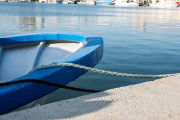 Fototapeta premium Stern of a blue fishing boat docked in port, tied with mooring lines, waterfront, sunny day, yachts in the background