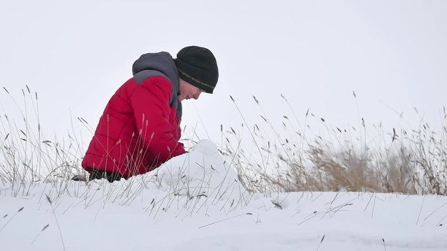 Teen boy rolling a ball of snow to build a fortress. sculpts winter snowman snow