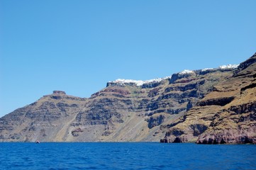 Fototapeta premium Waterless shore of the island of Santorini, Greece. Few people have adapted to live on this volcano. Sailing around the island by tour boat. From a trip to the Cycladic Archipelago
