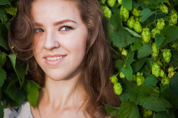 Young beautiful girl smiling in fresh green branches of hop, closeup portrait