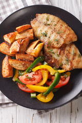 Grilled tilapia fillet, fried potatoes and a vegetable salad close-up. vertical top view