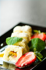 White sweet roll with kiwi, peaches, strawberries, mint. Serverd with almond peach and chocolate sauces on black plate. Sweet dessert for girl, woman, wife.