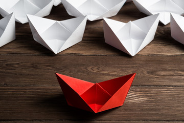 Business leadership concept with white and color paper boats on wooden table