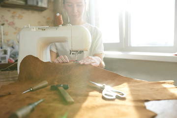 Female artisan threading brown leather on sewing machine, close up