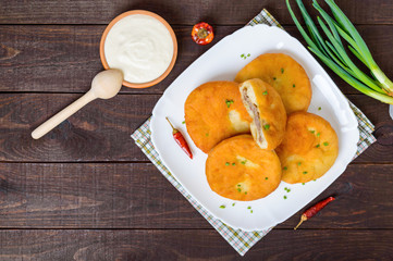 Deep frying pies with meat on a white plate with sour cream on dark wooden background. The top view