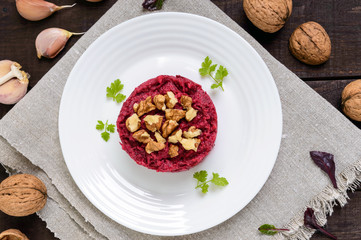 Vegetarian Lenten dish: a salad of beets with walnuts and garlic in a white plate in the shape of a circle on a dark wooden background. The top view.