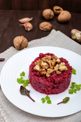 Vegetarian Lenten dish: a salad of beets with walnuts and garlic in a white plate in the shape of a circle on a dark wooden background. Vertical view