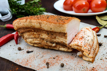 A large piece of bacon baked with spices and herbs on a paper with marinated tomatoes. The top view. A festive meal. Easter. Christmas.