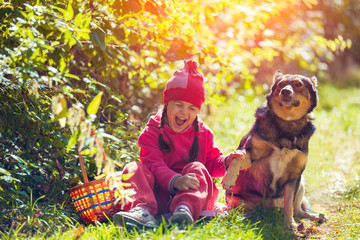 Fototapeta premium Happy little girl sitting with dog in the forest on picnic in sunny day.