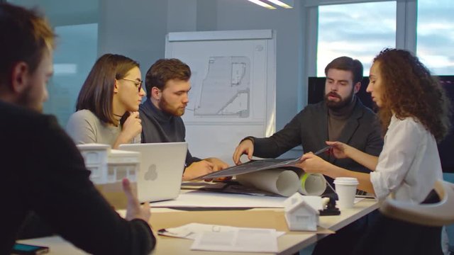 Slow motion of team of creative architects sitting behind table in conference room and discussing drafts for new project 