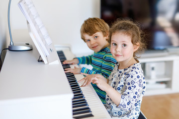 Two little kids girl and boy playing piano in living room or music school