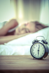 Young sleeping woman and alarm clock in bedroom at home