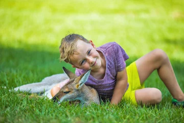 Photo sur Aluminium Kangourou Heureux garçon assis sur le sol et câlinant un kangourou australien