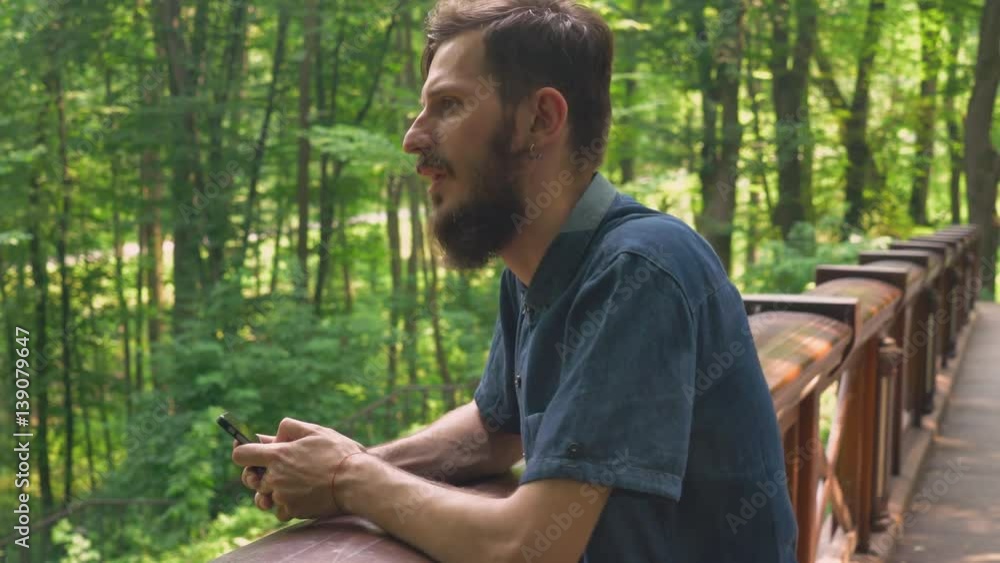 Poster a young bearded guy is holding a smarthone and laughing. he is texting a message or searching intern