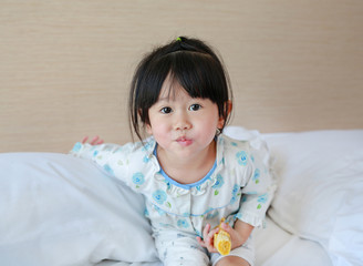 Cute Little girl in pajamas eating banana on the bed at the morning.