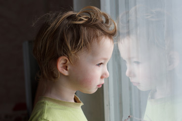 small boy sitting near window and thinking about something. He has beautiful great hair. Cute baby.