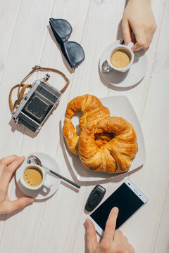 Hands holding espresso coffee cups and croissant on outdoor table with sun light
