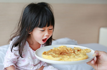 Little child girl looking Healthy breakfast with egg omelet on the bed.