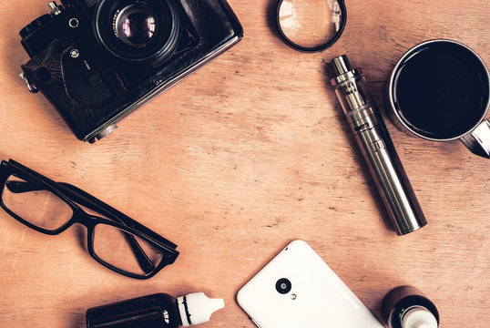 Vaping set, vintage camera, smartphone and coffee on the wood table. Hipster or bussinesman style. Trendy objects with copy space on the wooden background