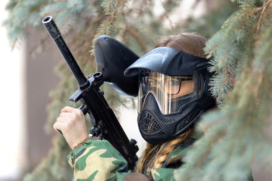 girl playing paintball in overalls with a gun.