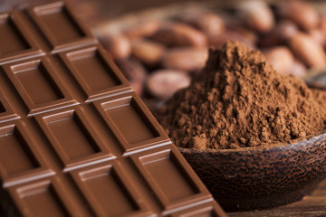 Chocolate bar, candy sweet, cacao beans and powder on wooden background
