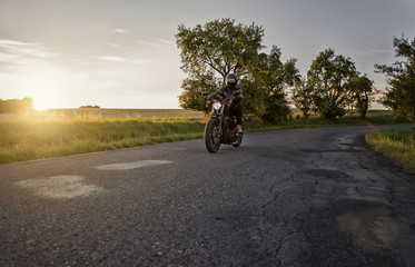 Chopper rider, biker, driving on a road during beautiful sunset. Biker season begins now during...