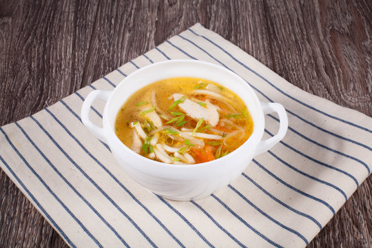 Chicken soup on a wooden background with a linen towel in a white tureen