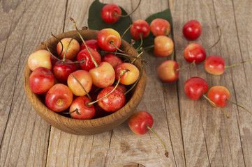 Background of ripe cherries. Pile of fresh and tasty cherries in wooden bowl. Fresh cherries scattered on a wooden table. Top view.