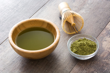 Matcha green tea in a bowl and bamboo whisk, on wooden background
