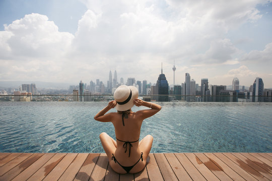 Woman in white hat sitting at Swimming pool on roof top with beautiful city view kuala lumpur Malaysia