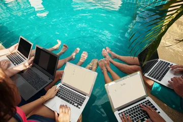 Foto op Plexiglas Group of people freelancers using laptop computer sitting near swimming pool and work together © Annatamila