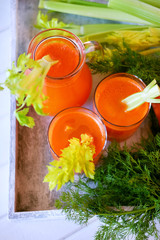 Fresh carrot juice poured into glasses and green celery