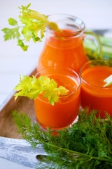 Fresh carrot juice poured into glasses and green celery